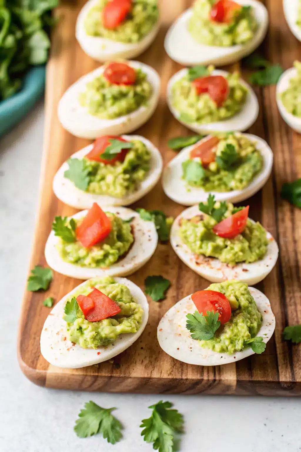 Avocado Deviled Eggs with a smooth, green filling, topped with diced tomatoes and cilantro.